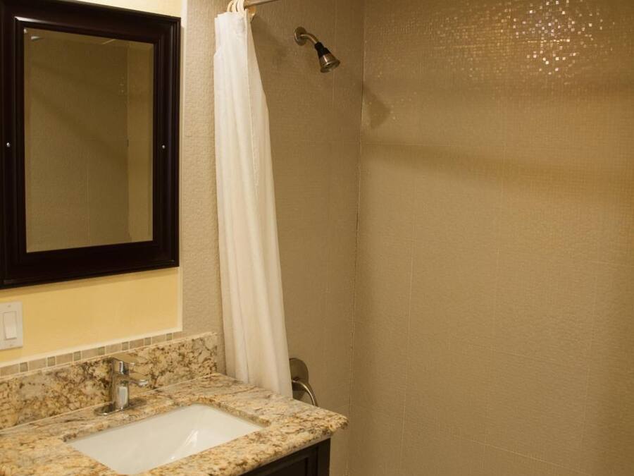 Un baño con lavamanos, espejo, ducha y una toalla colgada en la pared.