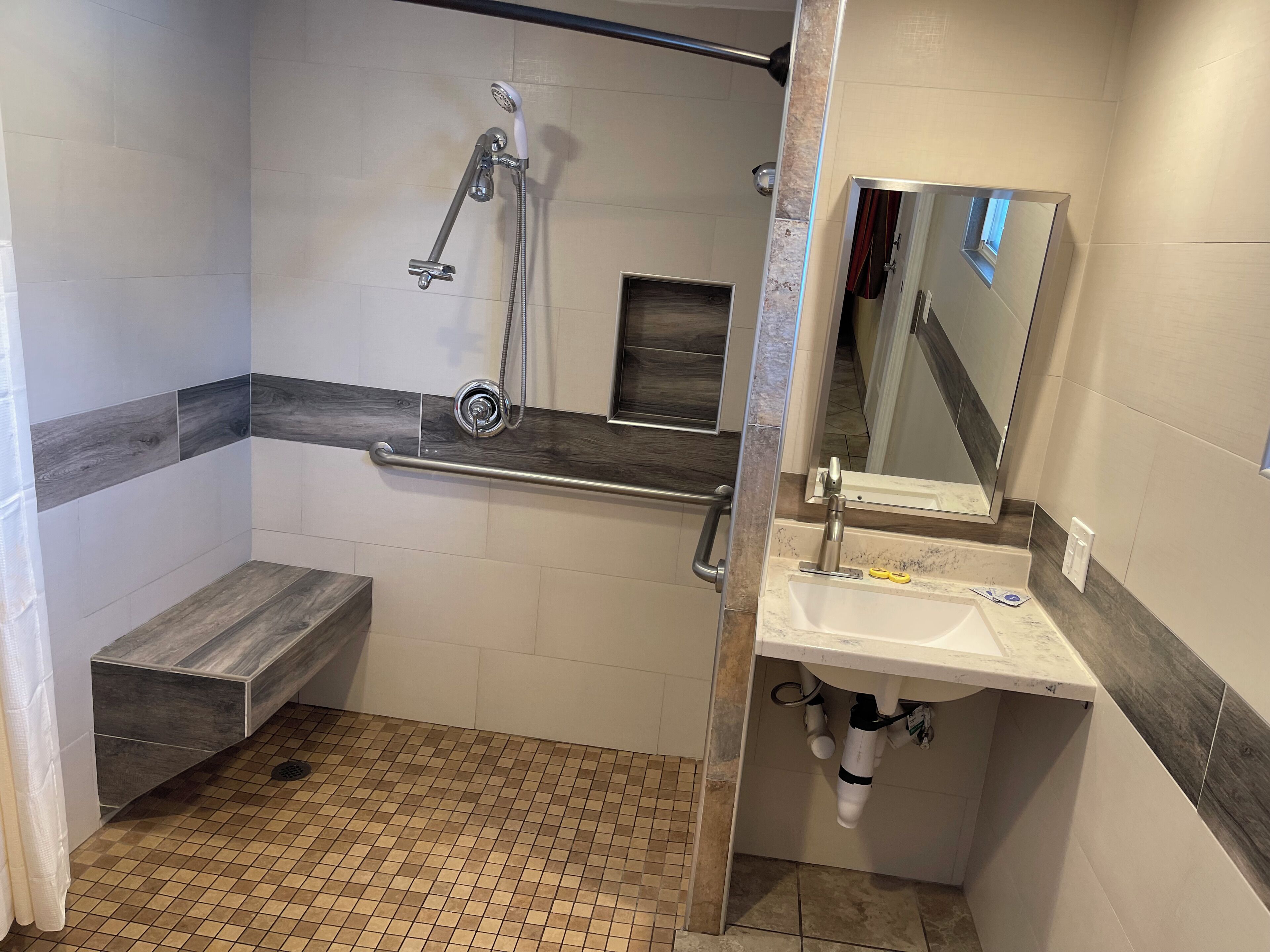 Un baño moderno con ducha, un banco, un lavamanos y un espejo.