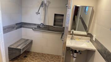 Un baño moderno con ducha, un banco, un lavamanos y un espejo.