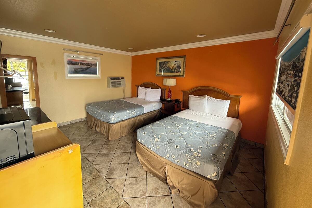 A hotel room with two beds, a desk, a window with a view, and a painting on the wall.