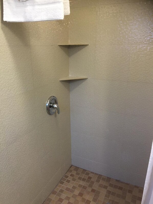 A small, tiled shower area with a single showerhead and two shelves mounted on the wall.