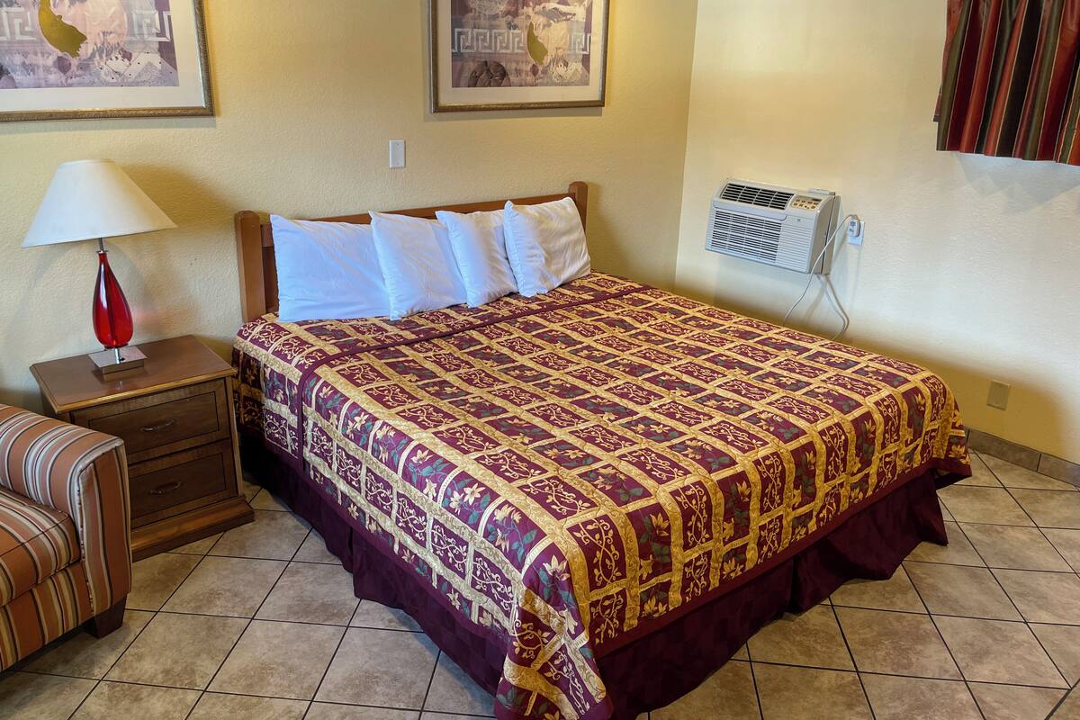 A hotel room with a bed, a nightstand with a lamp, a dresser, and two framed pictures on the wall.