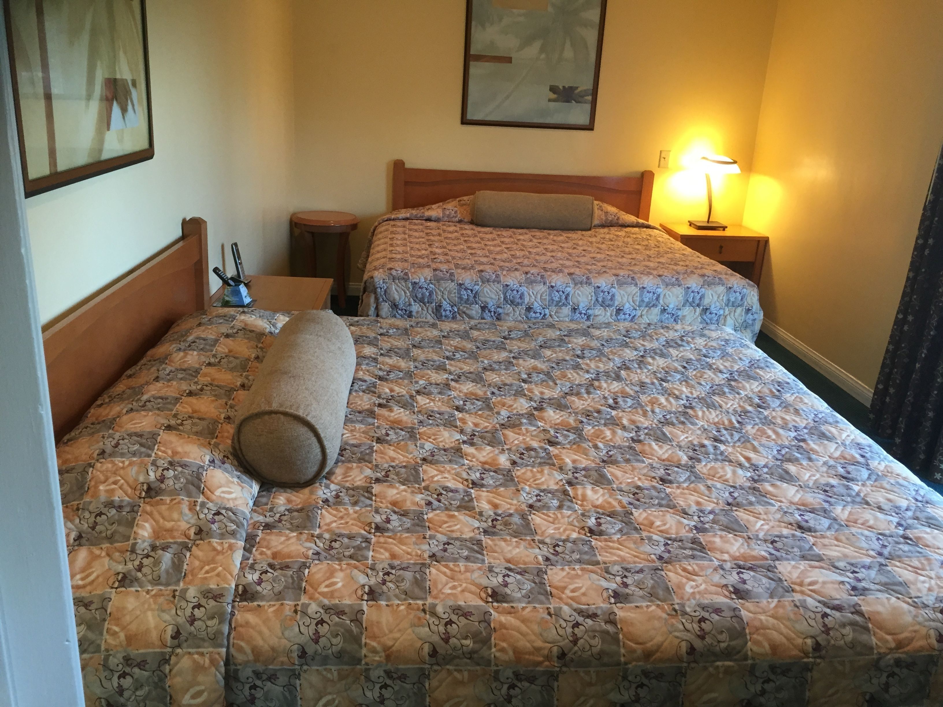 Ein Doppelbett mit einem gemusterten Bettbezug, eine Nachttischlampe und ein kleiner Tisch mit Tasse und Löffel.