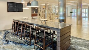 A modern lobby with a reception desk, bar stools, pendant lighting, and a large screen. - Fairfield Inn & Suites by Marriott Harrisburg West (New Cumberland)