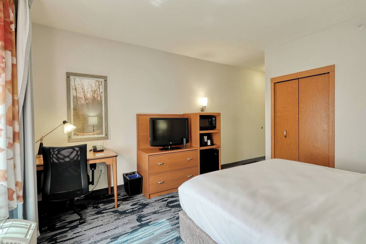 Una habitación de hotel con cama, escritorio, computadora, televisor y armario.