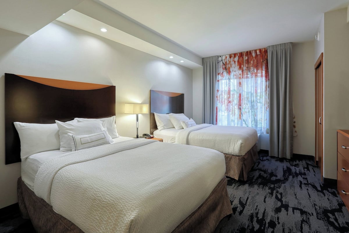 A hotel room with two beds, a large window with curtains, a desk, and a wardrobe.