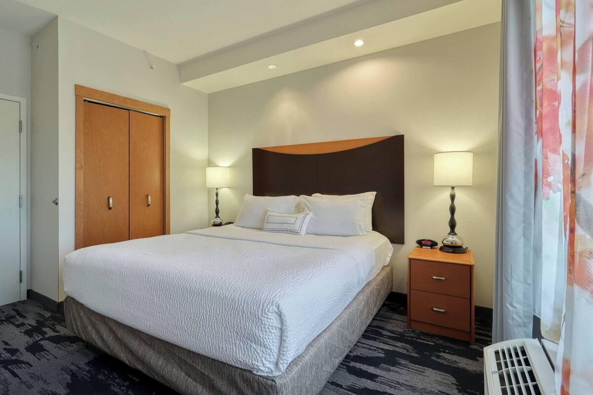 A hotel room with a large bed, two bedside tables with lamps, a wardrobe, and a vent.