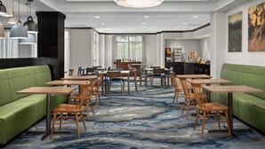 Uma área de refeições de hotel com sofás verdes, mesas e cadeiras de madeira, um grande candelabro e obras de arte nas paredes.