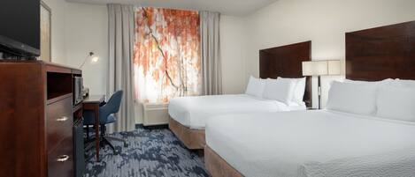 A hotel room with two beds, a desk, a TV, and a large window with curtains.