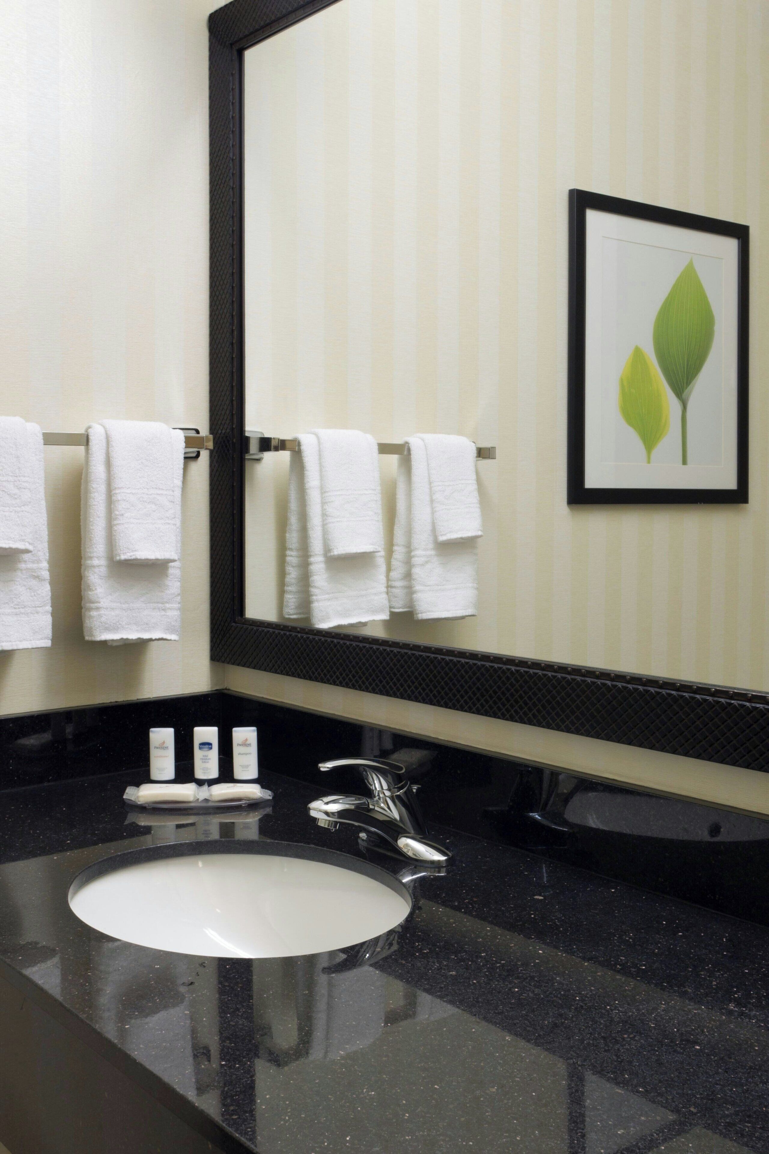 A bathroom with a black countertop, white sink, and a mirror. There are three white towels hanging on a rack.