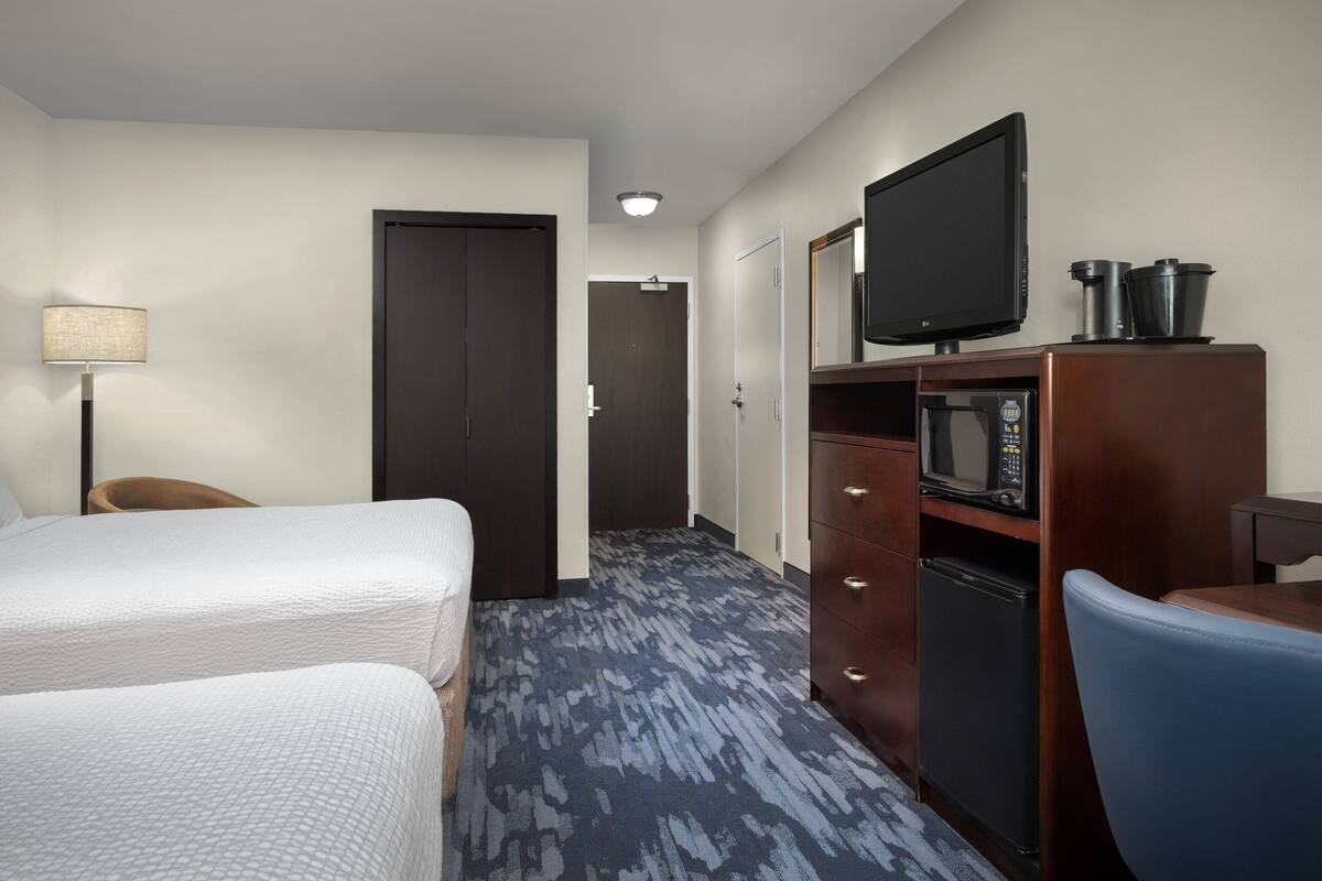 Ein Hotelzimmer mit zwei Betten, einem Schreibtisch mit Computer, einer Mikrowelle und einem Fernseher auf einer Holzkommode.