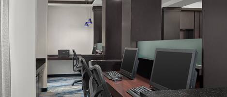 A modern office space with a long wooden desk, multiple computer monitors, and ergonomic chairs.