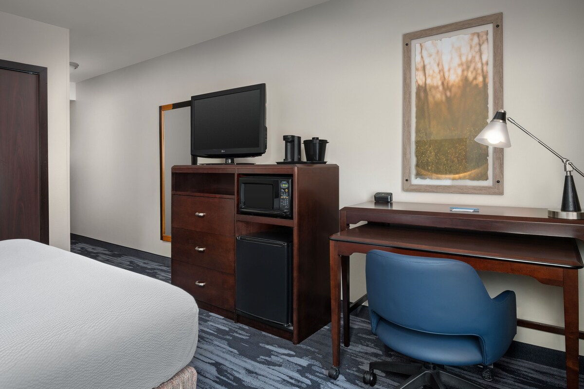 Une chambre d’hôtel équipée d’un lit, d’un bureau avec un ordinateur, d’une télévision, d’un four à micro-ondes, d’une machine à café et d’un tableau encadré au mur.