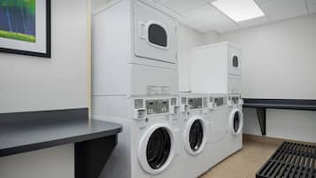 A laundry facility with stacked washing machines and dryers, a counter, and a wall-mounted picture.