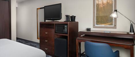 Quarto de hotel com cama, escrivaninha com computador, televisão, micro-ondas e cafeteira.