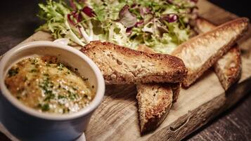 A wooden board with toasted bread, a bowl of sauce, and a mixed green salad.