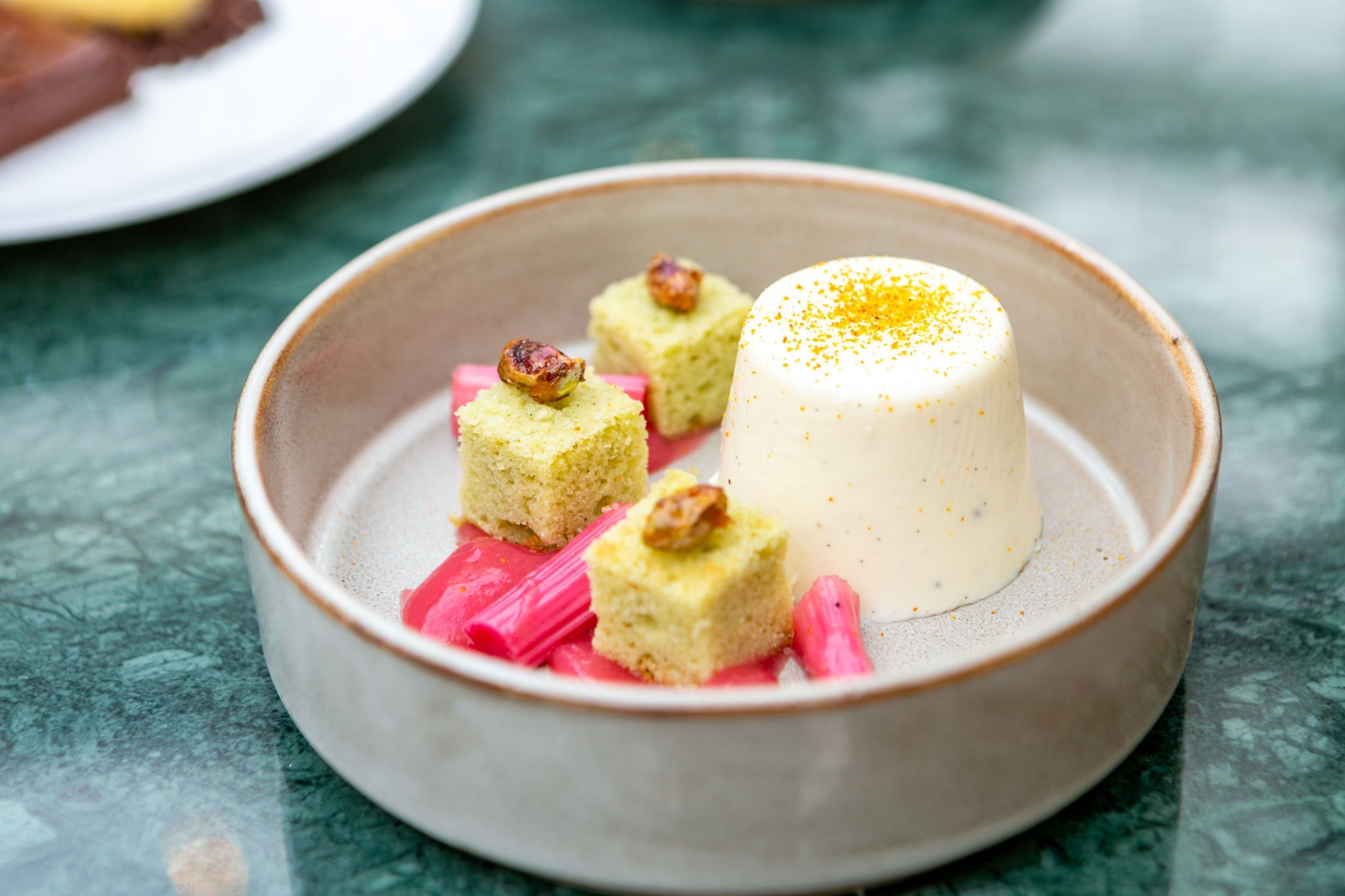 Une assiette à dessert sur laquelle on trouve une pâtisserie blanche en forme de sphère et de petits morceaux carrés, dont certains sont parsemés de noix, le tout présenté sur une assiette en céramique.