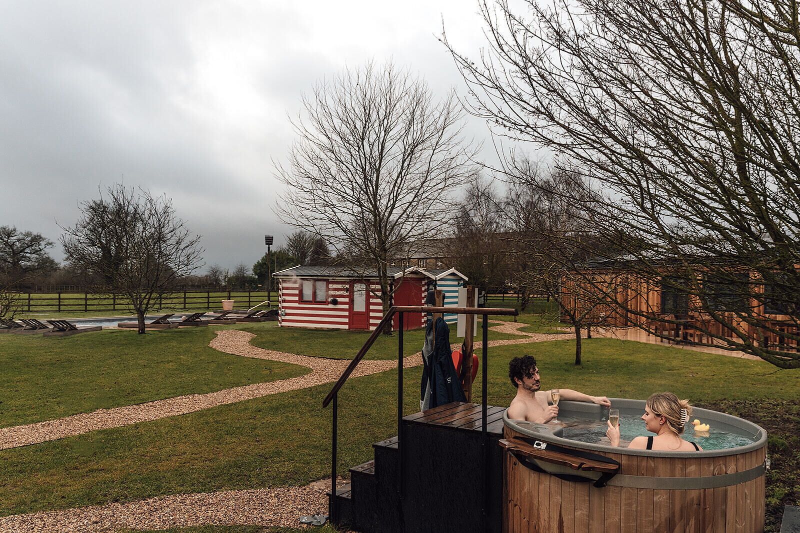 A hot tub area with a wooden deck, a small red and white striped building, and a fenced yard.