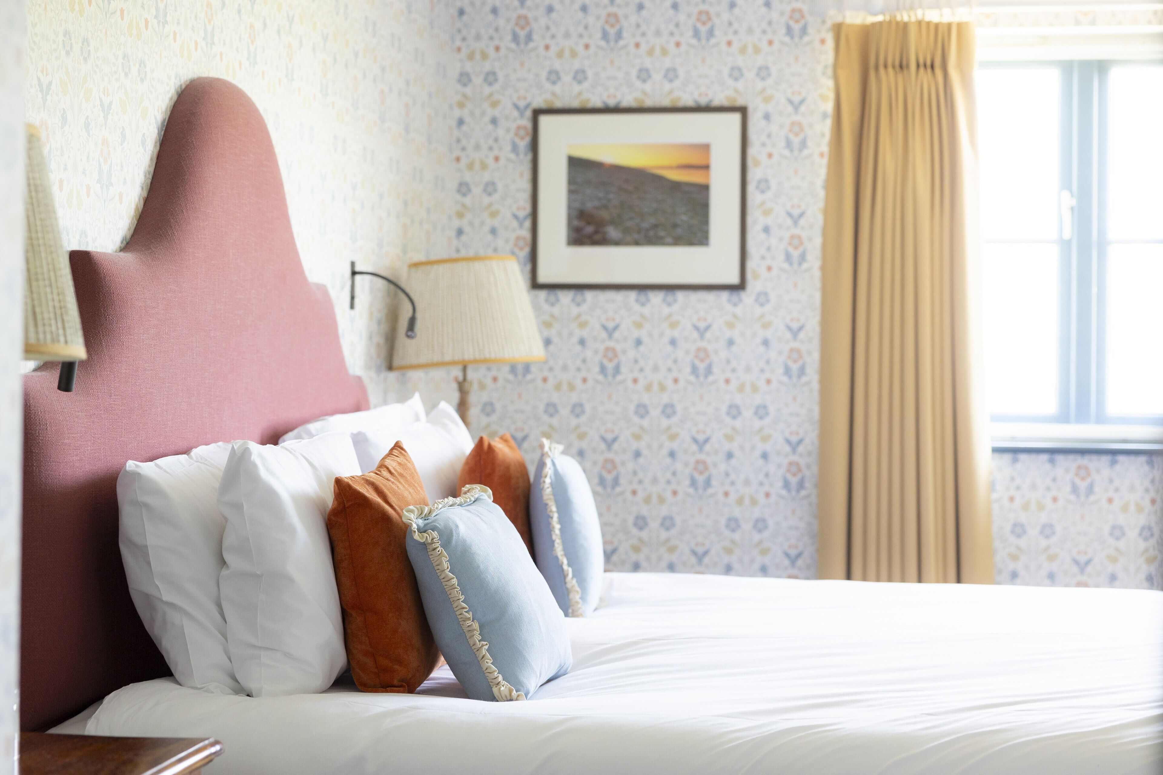 A neatly made bed with white and brown pillows, a pink headboard, and a framed picture on the wall.