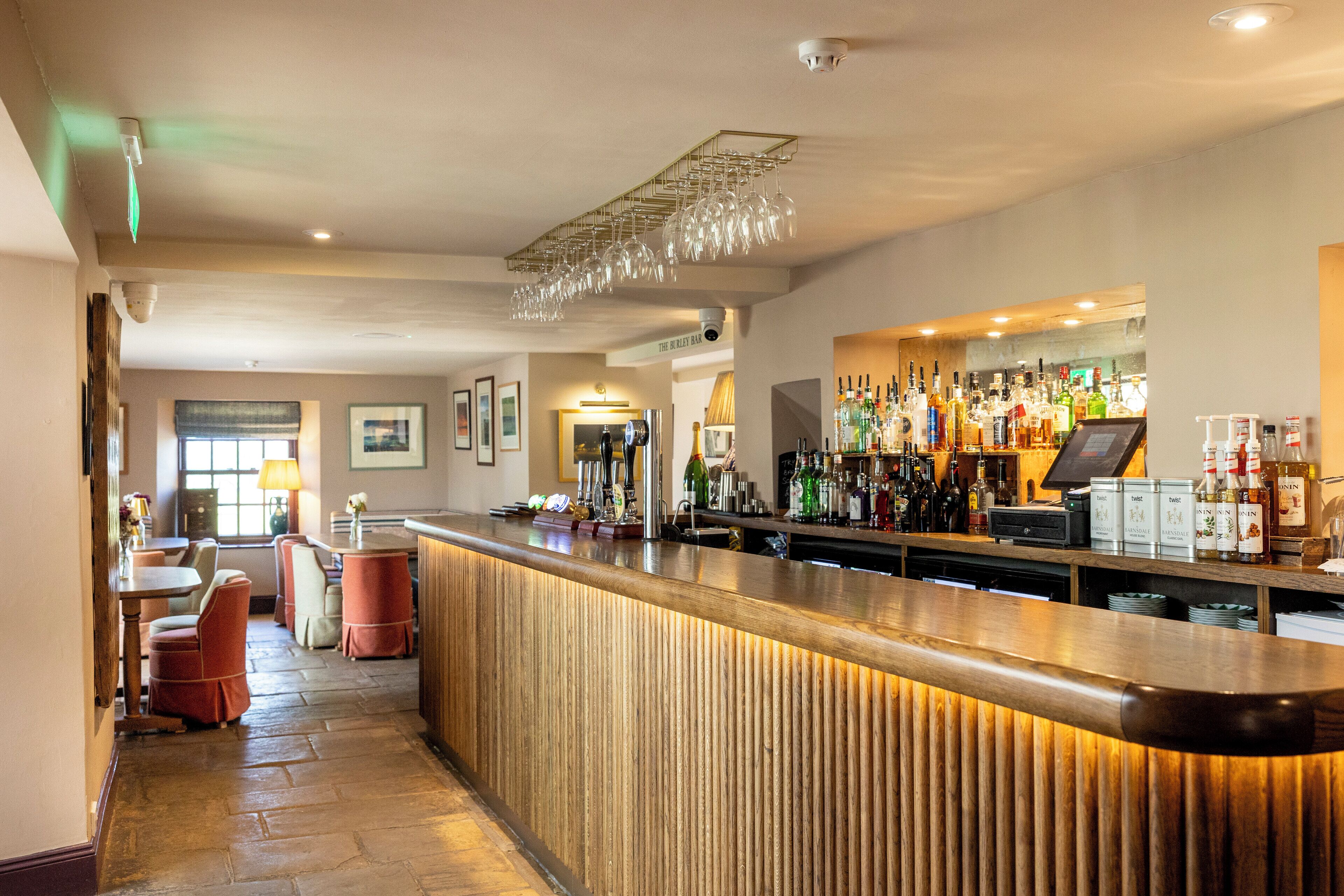 A bar area with a wooden counter, seating, and a variety of bottles and glasses.