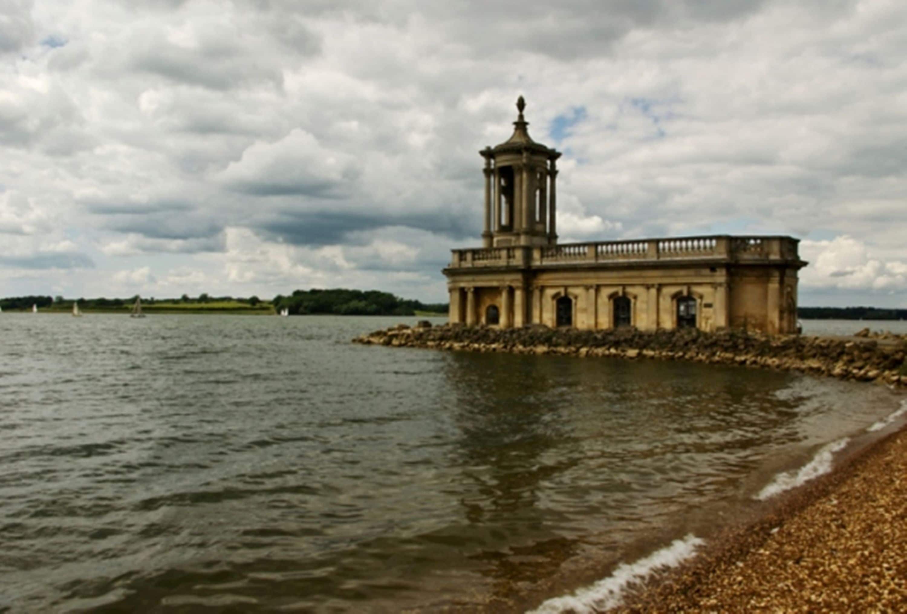 A historic building with a tower, situated on a rocky outcrop by a body of water.