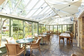 A conservatory with glass walls, wicker furniture, and stone flooring. - The Barnsdale, Rutland (Oakham)
