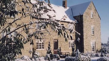Un edificio de piedra con fachada simétrica, ventanas amplias y tejado cubierto de nieve.