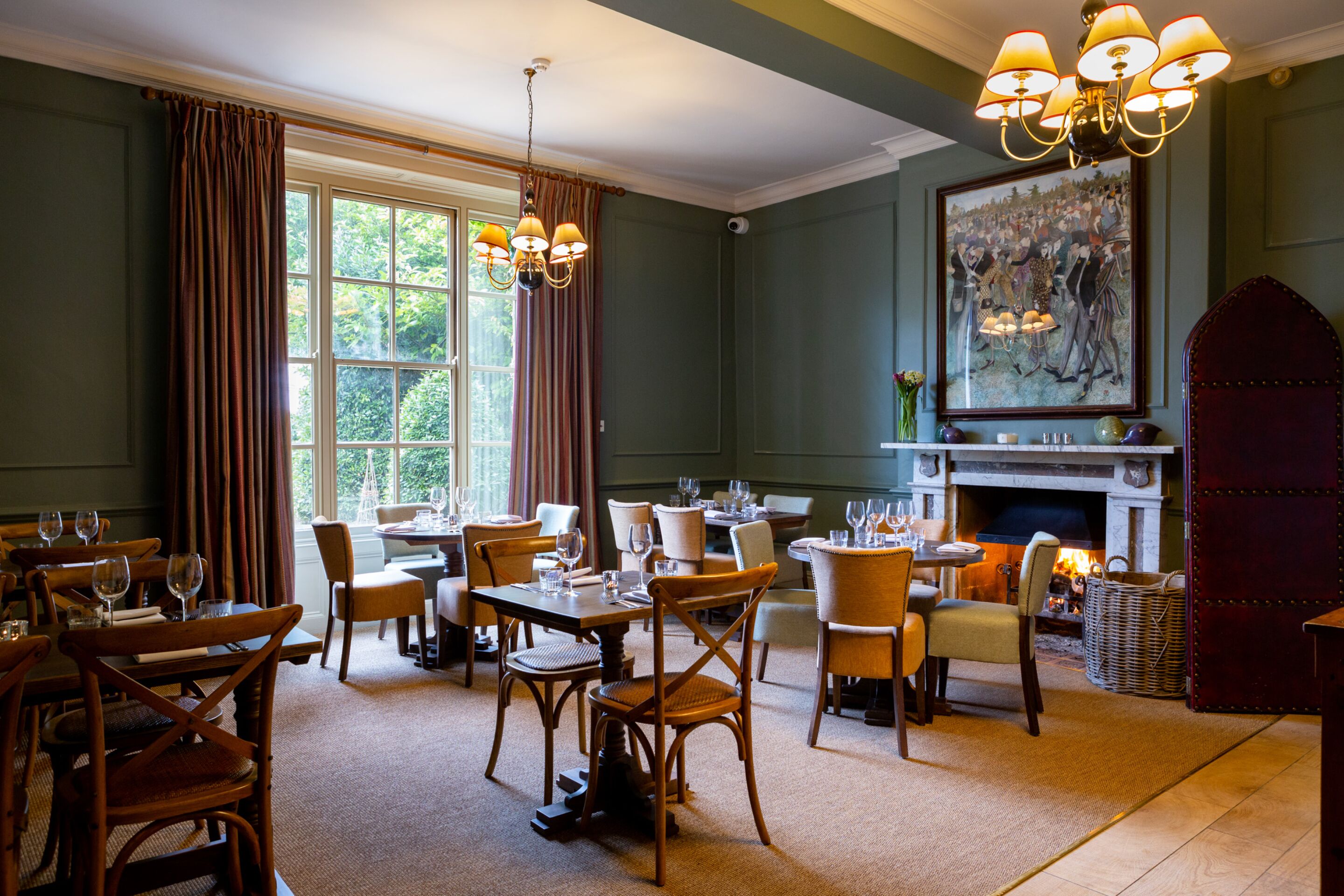 A dining area with multiple tables and chairs, a fireplace, and a large painting on the wall.