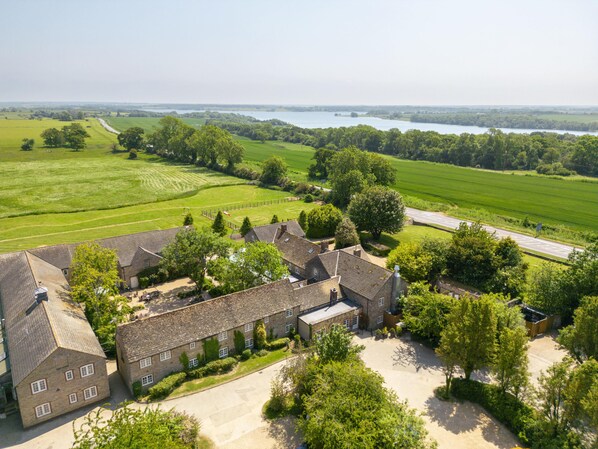 A traditional stone building with a courtyard, surrounded by lush green fields and a river in the background. - The Barnsdale, Rutland (Oakham)