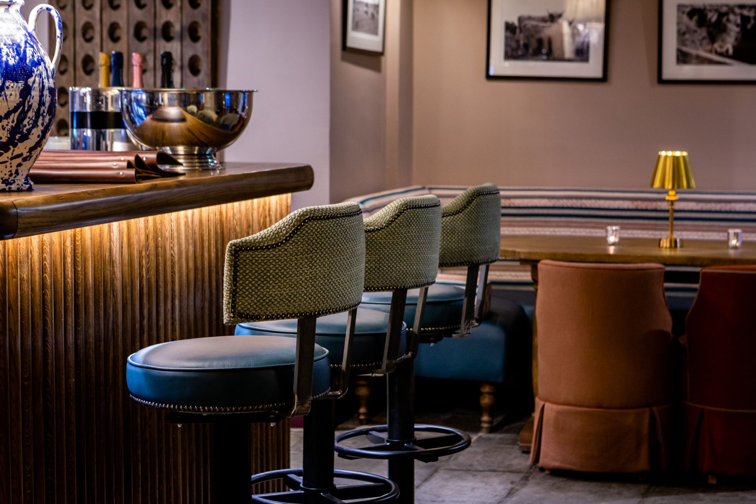 A bar area with stools, a bar counter, and a table with a lamp.