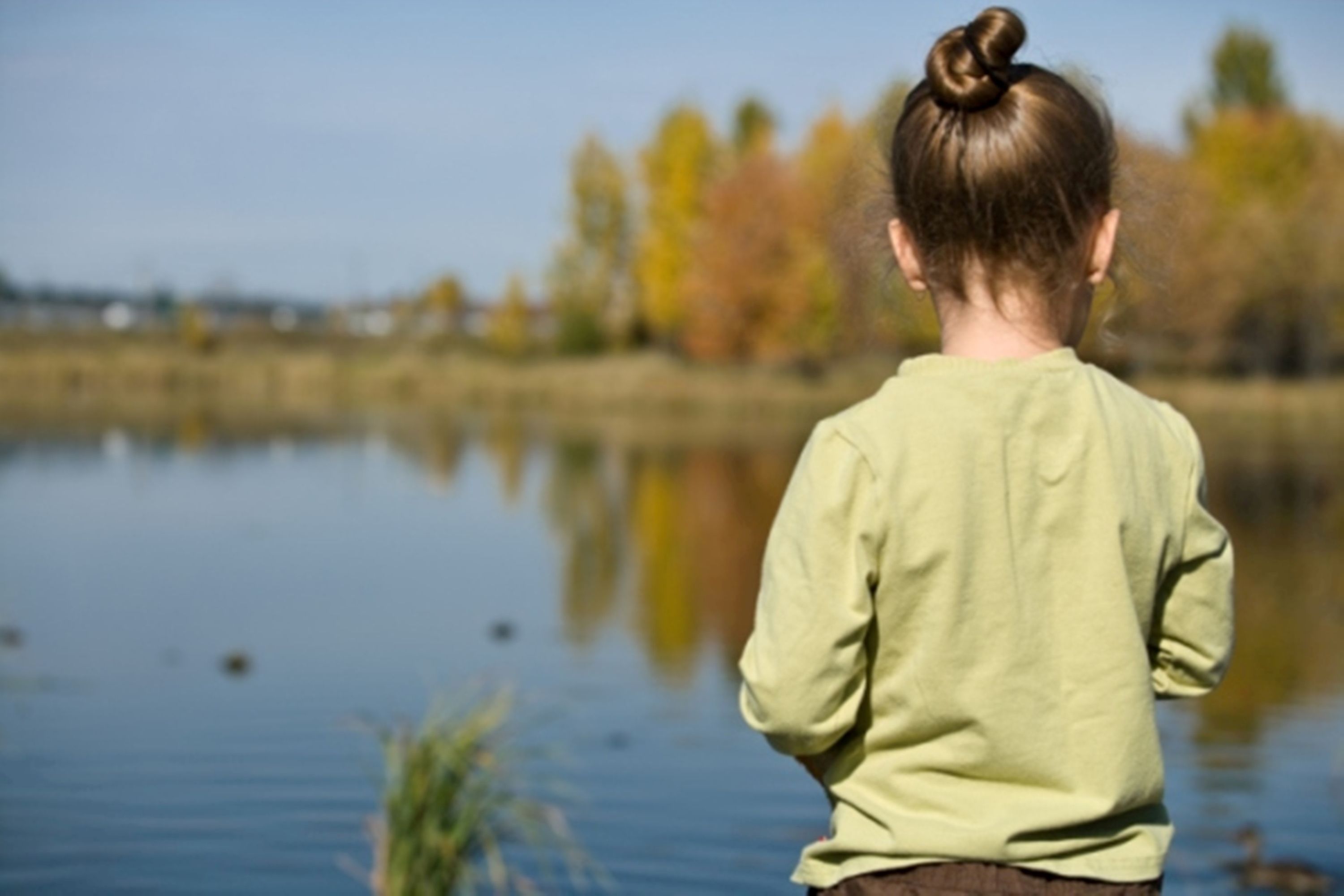 A person standing by a calm body of water with trees in the background.