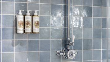 A bathroom with a tiled wall, a showerhead, and three bottles of shampoo and conditioner.