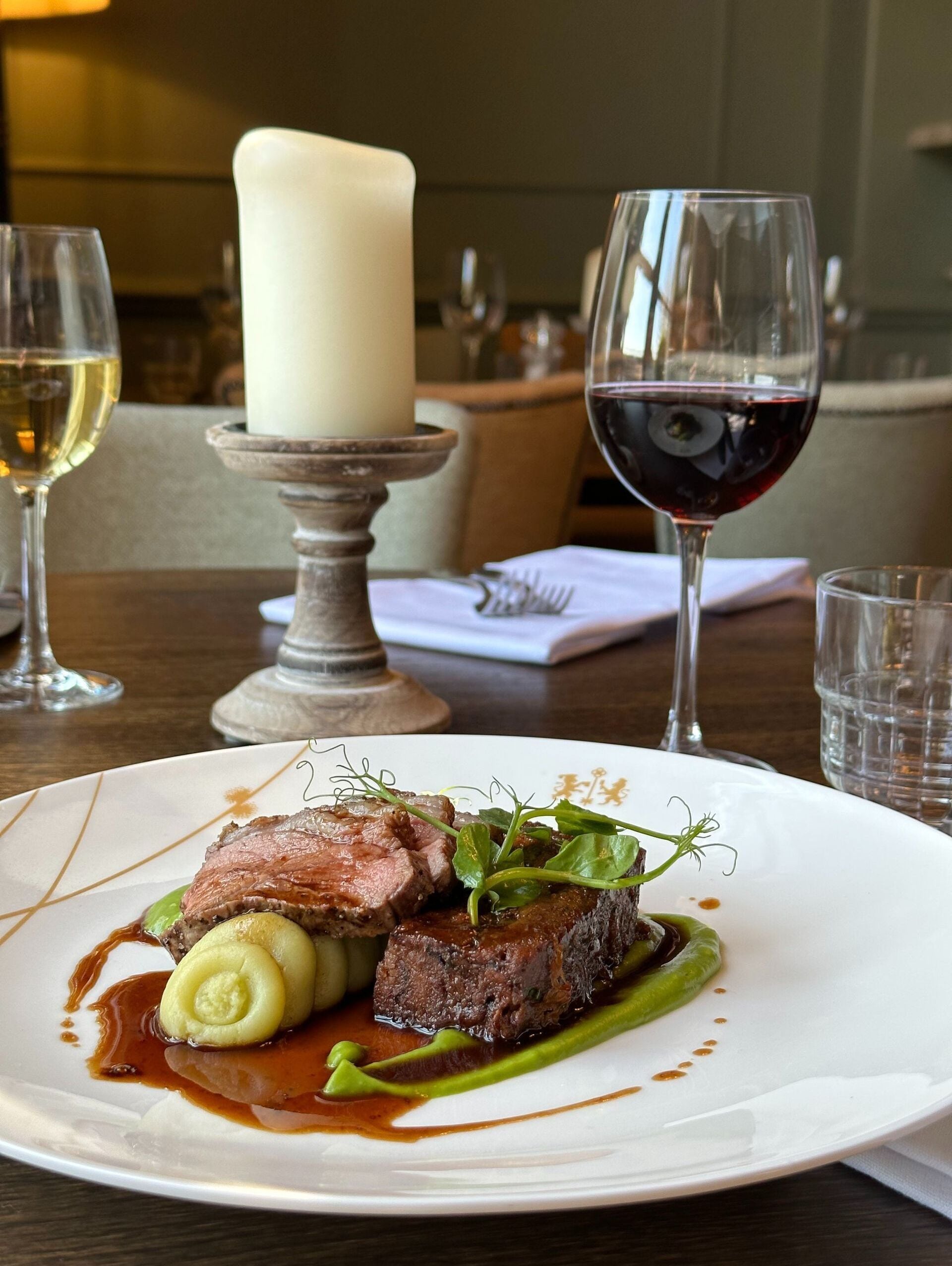 A plate of food with a candle and wine glasses on a table.