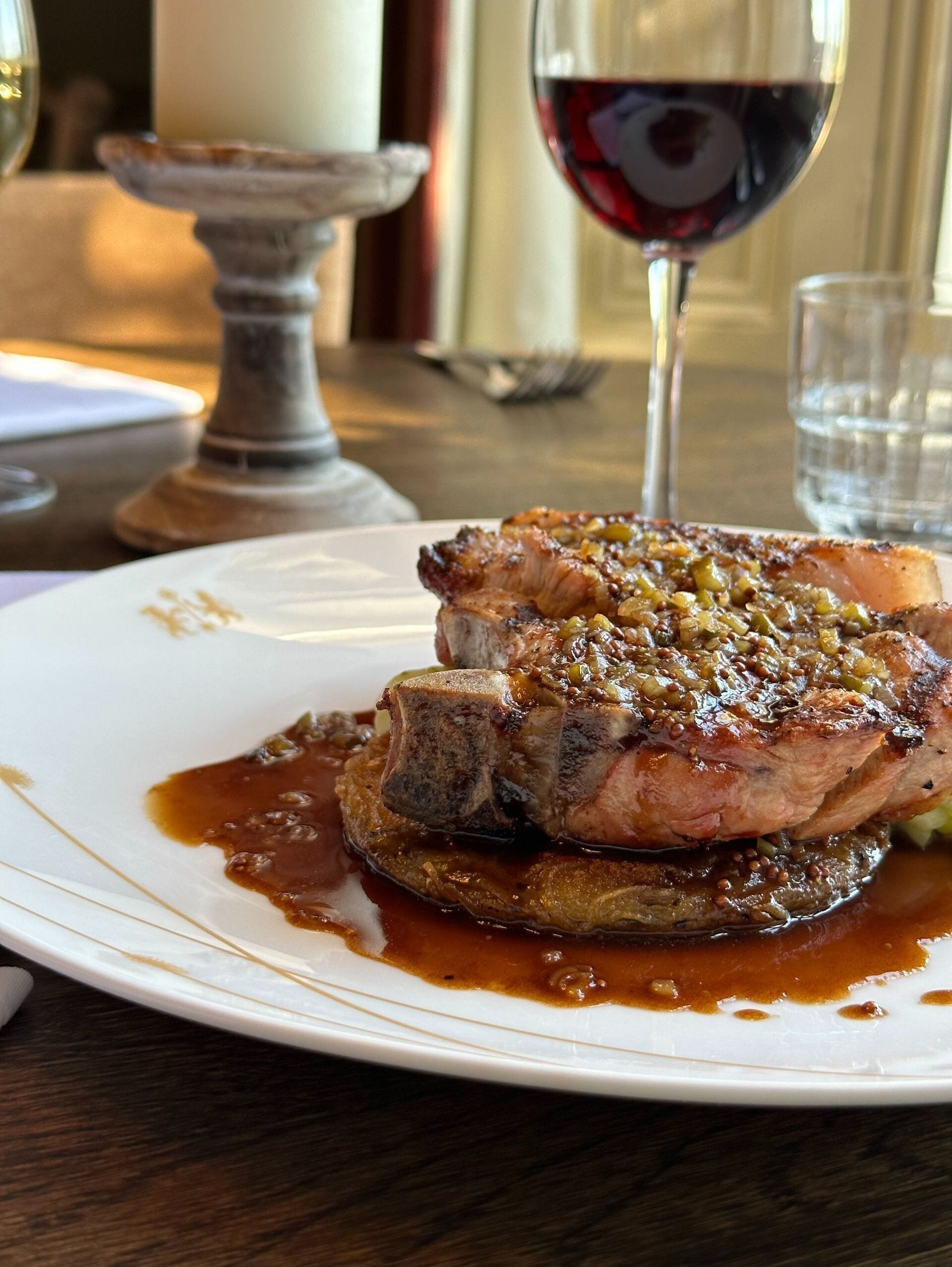 A plate of food with a steak and sauce, a wine glass, and a candle on a table.
