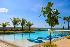 Uma piscina com espreguiçadeiras azuis, palmeiras e um céu azul límpido.