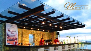A bar with a stone facade and a glass canopy, overlooking a body of water. - Ciriaco Hotel and Resort (Calbayog)