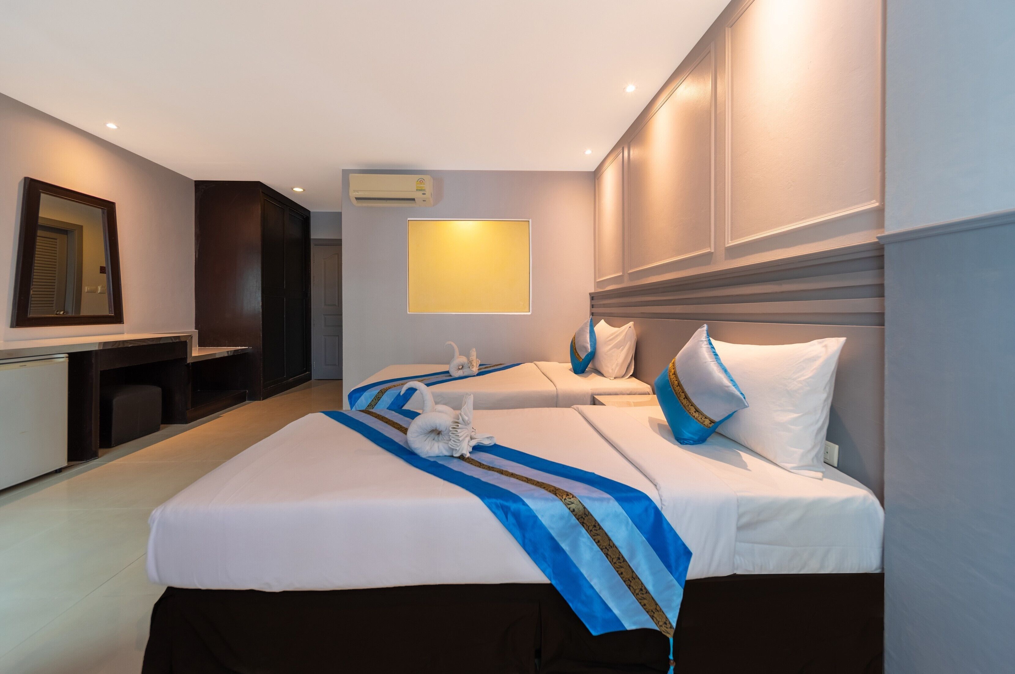 A hotel room with two beds, a desk, and a mirror.