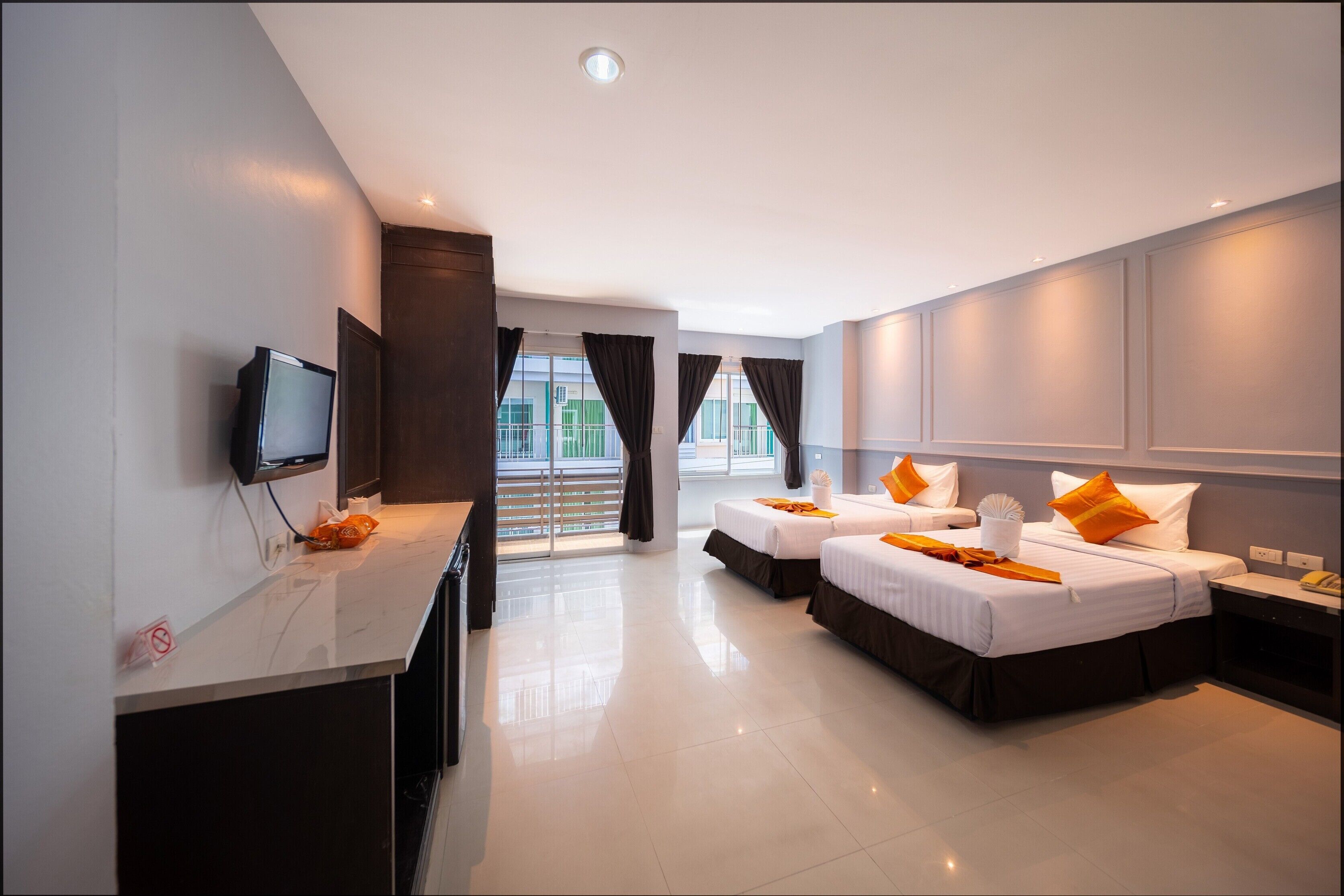 A hotel room with two beds, a TV, a desk, and a balcony with curtains.