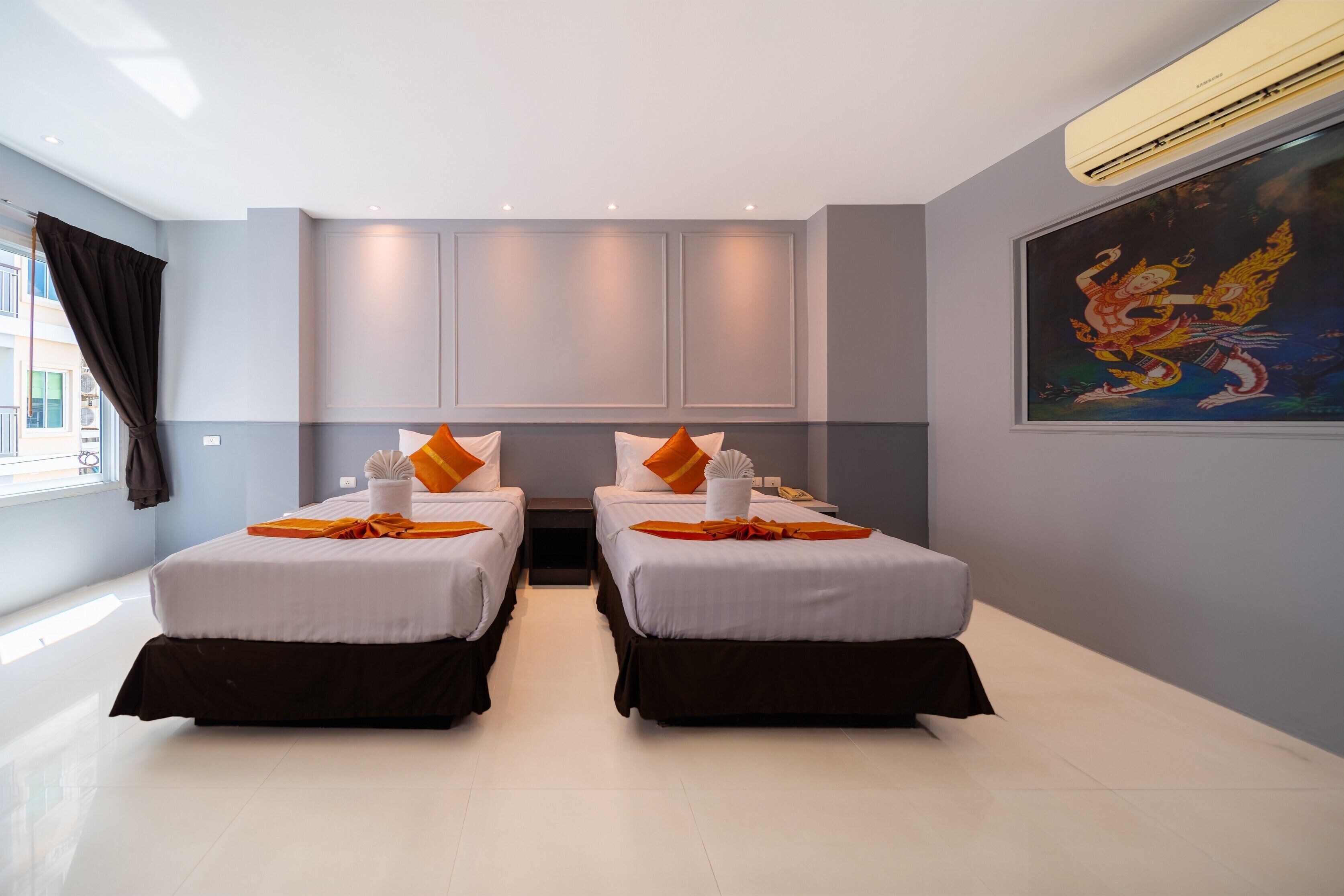 A hotel room with two beds, a large window with curtains, a painting on the wall, and an air conditioning unit.