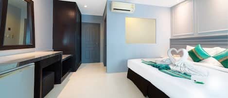 A hotel room with a bed, a desk, a mirror, and an air conditioning unit.