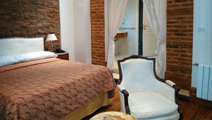 A bedroom with a brick wall, a bed with a patterned bedspread, a white chair, and a canopy over a door. - Hotel AyB Internacional (Buenos Aires)