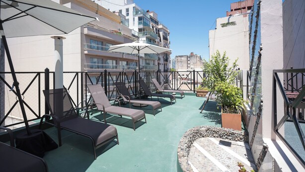 A rooftop terrace with lounge chairs and umbrellas, a pool, and a view of surrounding buildings. - Hotel AyB Internacional (Buenos Aires)