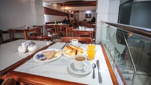 A dining area with marble tables, wooden chairs, and breakfast items like croissants, orange juice, and coffee. - Hotel AyB Internacional (Buenos Aires)