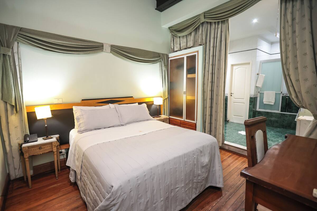 Une chambre d’hôtel comprenant un lit, une table de chevet, une lampe, une chaise en bois et une armoire.