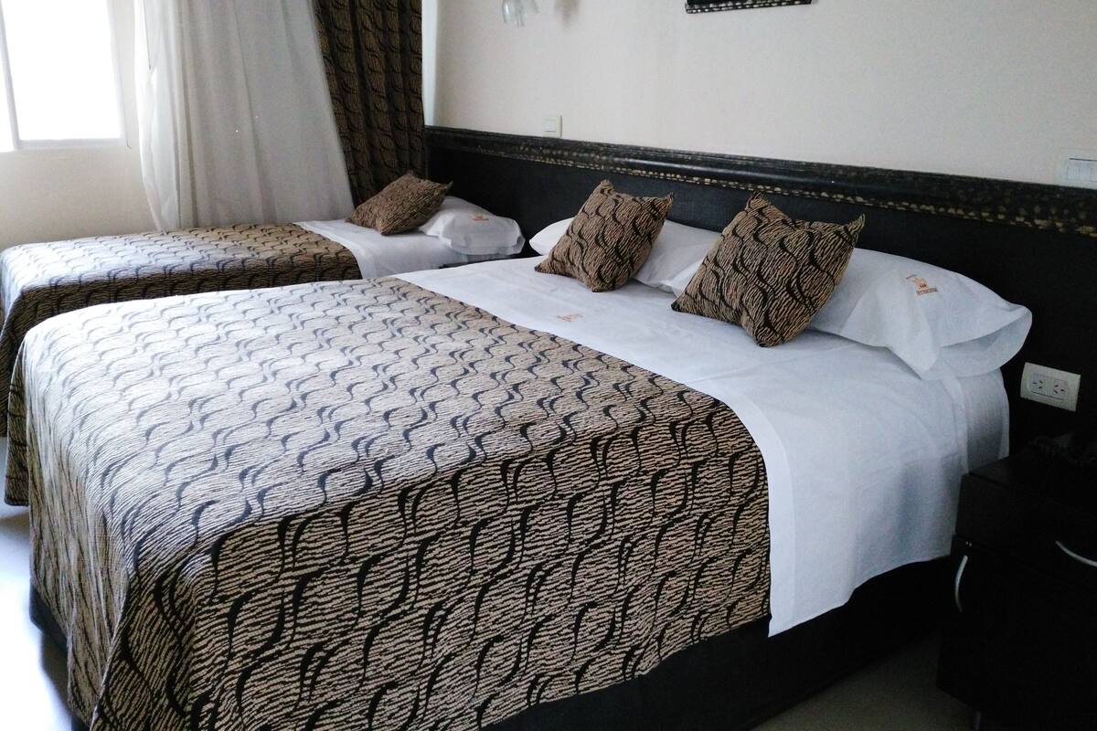 Une chambre d’hôtel avec deux lits, chacun recouvert d’une couvre-lit à motifs et agrémenté d’oreillers assortis. Un luminaire mural et un tableau encadré sont fixés au mur au-dessus des lits.