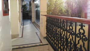 A corridor with a tiled floor, a black wrought iron railing, and a sign indicating a room number. - Hotel AyB Internacional (Buenos Aires)
