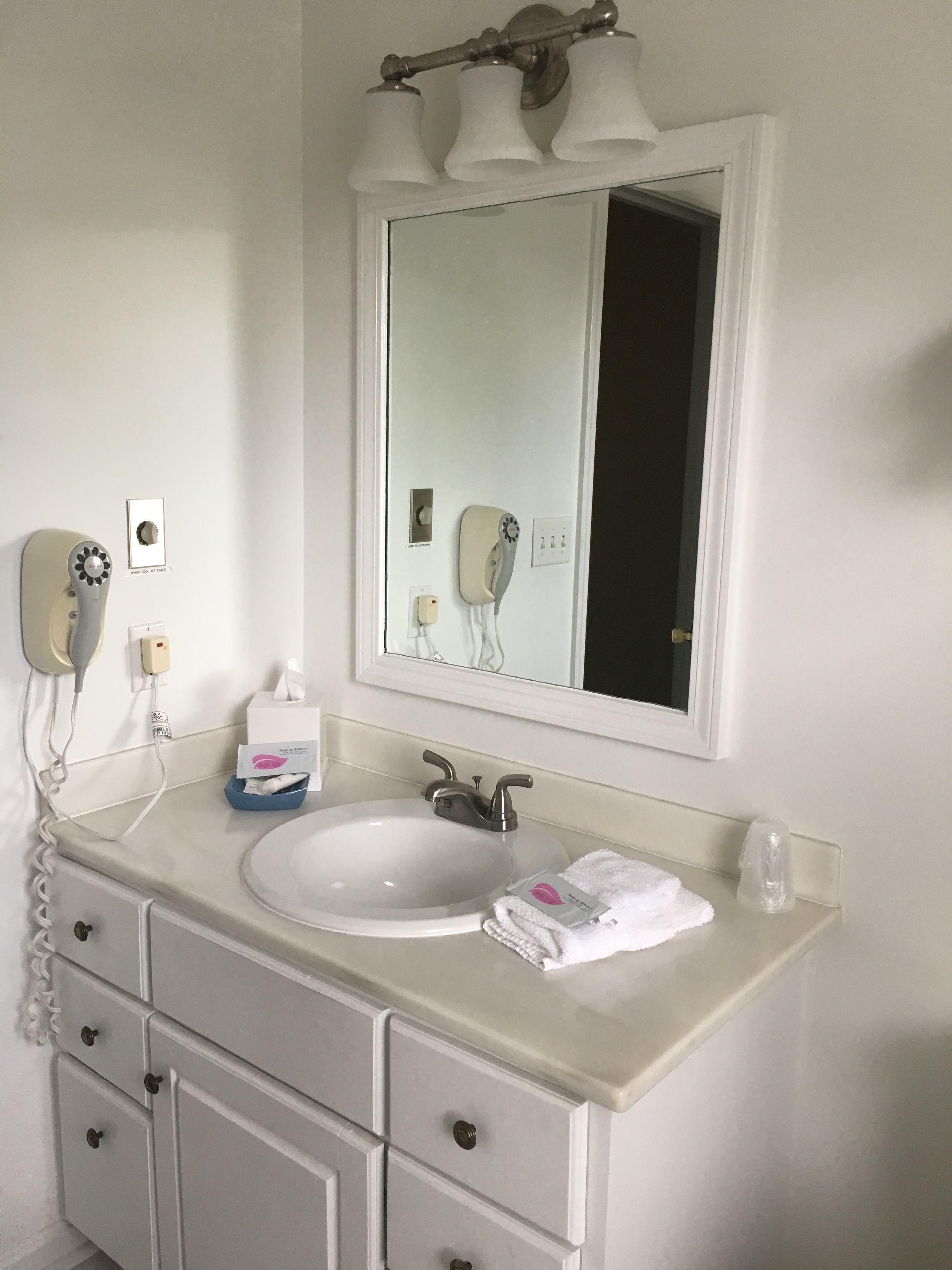 Une salle de bain avec un lavabo blanc, un miroir, une serviette et un sèche-cheveux fixé au mur.