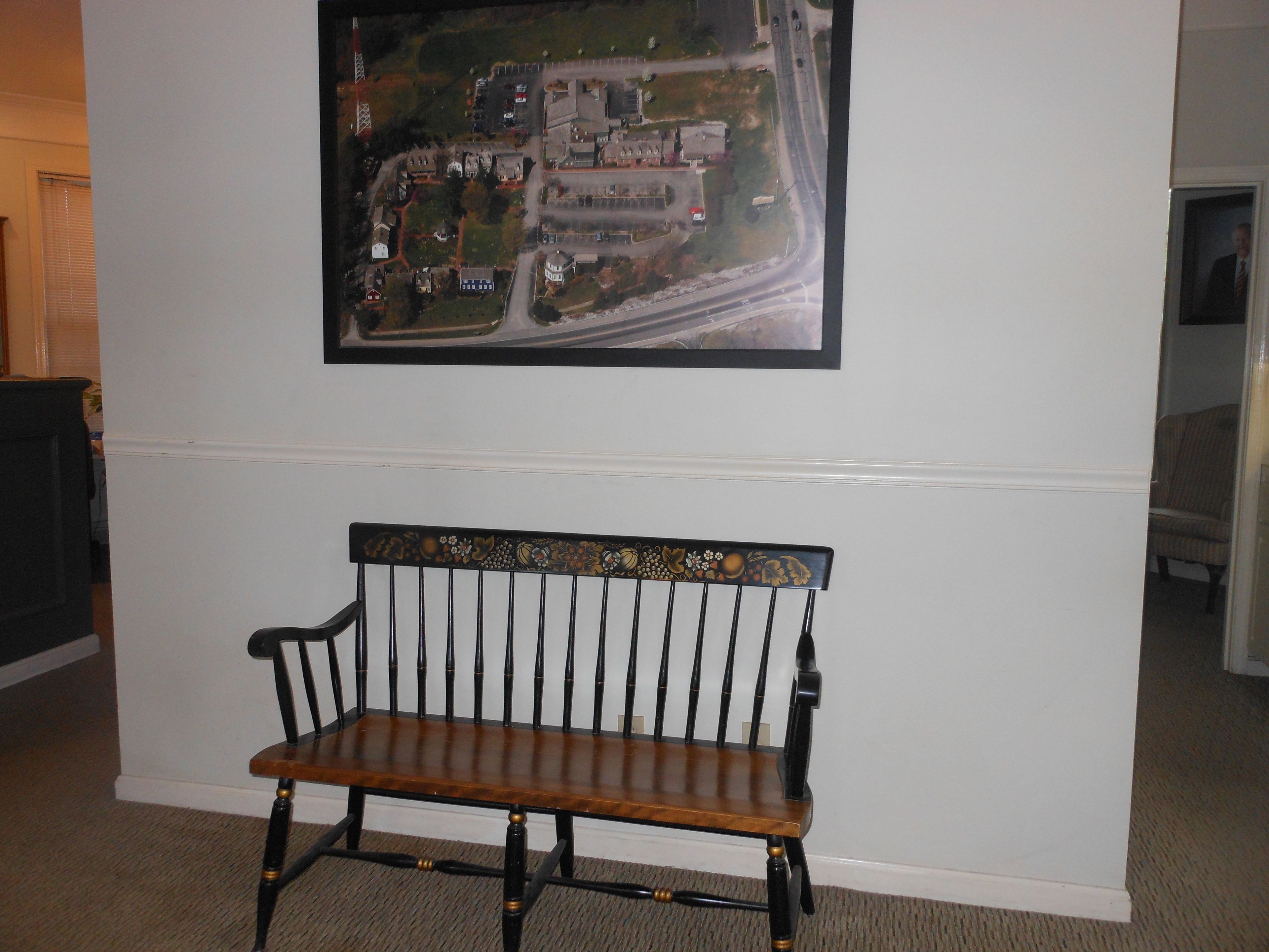 A room with a wooden bench, a framed aerial photograph on the wall, and a carpeted floor.