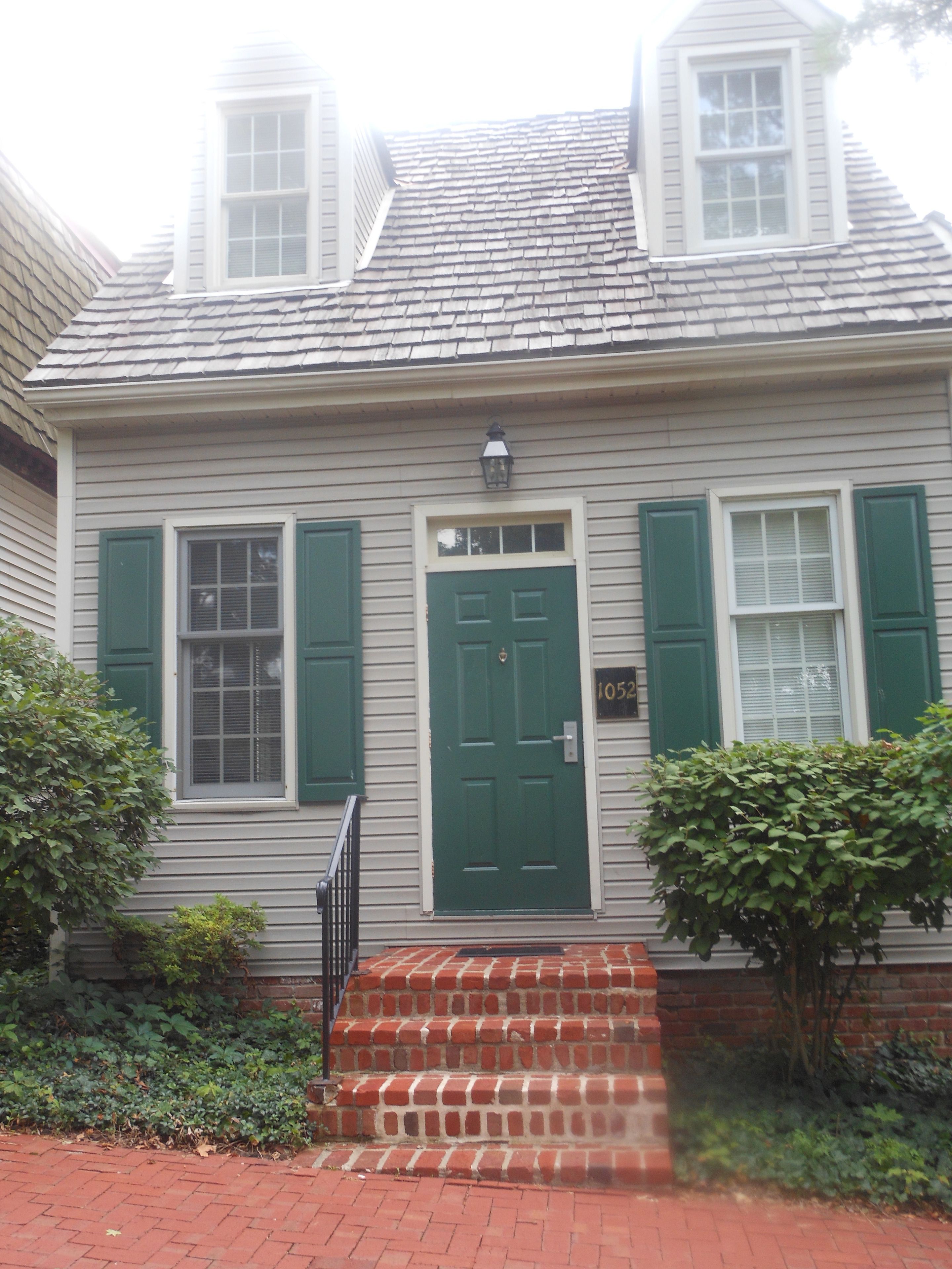 A two-story house with a green door, white shutters, and a brick staircase leading to the front door.