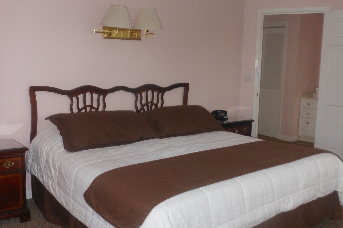A bedroom with a single bed, a nightstand, a lamp, and a door.